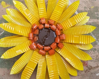 May include: A yellow metal sunflower with a brown centre and orange petals. The sunflower is made from recycled materials and has a rustic, handmade look.