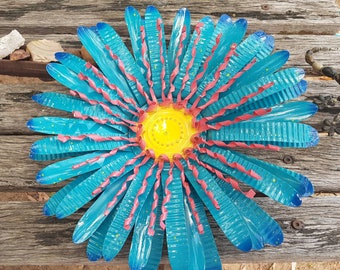 May include: A blue and pink metal flower with a yellow centre. The flower is made from recycled materials and has a rustic, handmade look.
