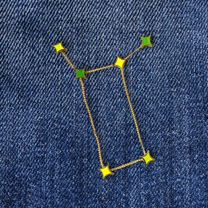 May include: A gold chain with yellow and green star-shaped charms arranged in the shape of the Gemini constellation.
