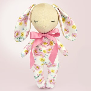 May include: A plush bunny toy with a floral print fabric. The bunny has a pink bow and closed eyes.