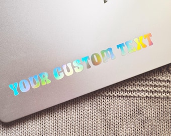 May include: A silver laptop with a holographic sticker that says "YOUR CUSTOM TEXT" in rainbow colors.