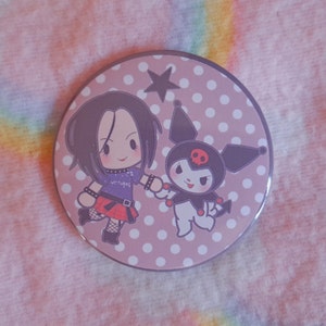 May include: A circular badge with a light purple background and white polka dots. The badge features two cartoon characters holding hands. One character has black hair and a purple top. The other is black and white with a red skull.