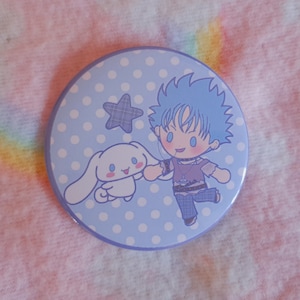 May include: A circular badge with a light blue background and a cartoon illustration. The design features a blue-haired character and a white bunny-like creature holding hands. A plaid star and white polka dots are also included.