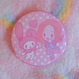 May include: A circular pink badge featuring a cartoon illustration of a girl and a bunny. The badge has a pink polka dot background and a pink border. The girl has red hair and is wearing a blue and pink outfit. The bunny is pink.