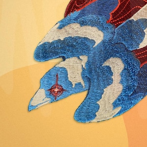 May include: Embroidered iron-on patch featuring a blue and white bird with a red flame design. The bird is flying with its wings spread out. The patch is perfect for adding a unique touch to clothing, bags, or other fabric items.