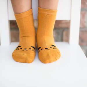 Könnte beinhalten: Ein Paar gelbe Socken mit einem schwarzen Katzenkopf-Design an den Zehen.