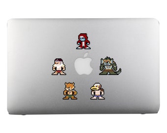 Op de afbeelding: Vijf pixel art karakterstickers zijn geplaatst op een zilveren laptop. De stickers tonen verschillende karakters, waaronder een rood geklede figuur, een gespierde krijger, een eend, een eekhoorn en een bebaarde man. Elk karakter heeft een uniek ontwerp en kleurenschema.