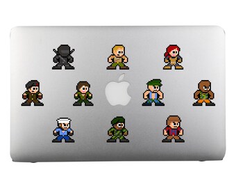 Op de afbeelding: Een zilveren laptop met tien pixel art stickers van personages in verschillende poses en outfits. De personages dragen militaire uniformen, camouflage en een ninja-pak. De laptop heeft een Apple-logo.