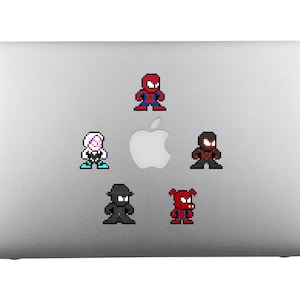 May include: A silver laptop with five pixelated superhero stickers. The stickers are of Spider-Man, Spider-Gwen, Miles Morales, and two other black and red Spider-Man characters.