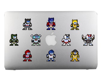 Op de afbeelding: Een zilveren laptop met negen pixel art stickers van Transformers-personages. De personages staan in verschillende poses en kleuren, waaronder rood, blauw, geel, groen en zwart.