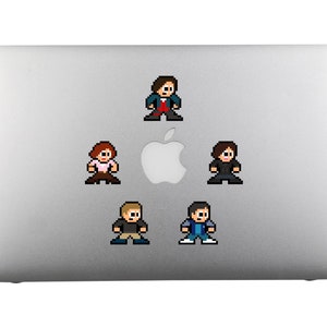 May include: Five pixel art stickers of characters from a television show are placed on a silver laptop. The characters are wearing different coloured clothing and are in various poses.