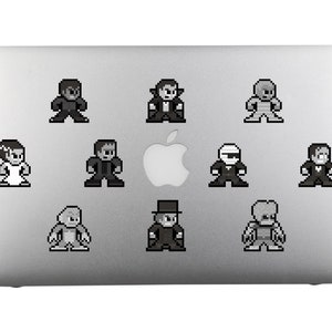 Può includere: Un laptop argentato con nove adesivi in pixel art in bianco e nero di personaggi classici dei film horror. I personaggi includono il mostro di Frankenstein, Dracula, il lupo mannaro, la mummia, la creatura della laguna nera e altri.