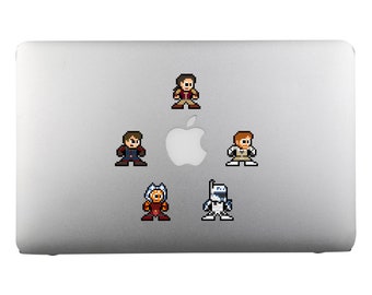 Op de afbeelding: Een zilveren laptop met vijf pixel art stickers van personages uit een sciencefictionfilm. De stickers zijn van een man in een bruin jack, een man in een blauw jack, een man in een wit shirt, een vrouw in een rood-oranje outfit en een robot in een wit-blauw pak.