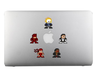 Op de afbeelding: Een zilveren laptop met vijf pixel art stickers van superhelden. De stickers zijn van Ghost Rider, Daredevil, Punisher, Elektra en een personage met een schedel en gekruiste beenderen.