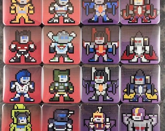 May include: A set of sixteen square magnets featuring pixel art characters. Each magnet displays a unique robot figure in a distinct colour scheme, including yellow, red, blue, green, and purple. The designs are arranged in a four-by-four grid.