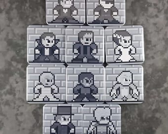 Op de afbeelding: Een verzameling van tien vierkante buttons met speld, voorzien van pixel art-illustraties van klassieke horrorfilmpersonages. Elke button toont een personage tegen een achtergrond van een lichtgrijze bakstenen muur in zwart, wit en grijs.