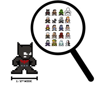 Op de afbeelding: Een pixel art-figuur van Batman, staand met gekruiste armen, draagt een zwart pak met een rood vleermuis-symbool op de borst. Het figuur is 1,27 cm breed. Een vergrootglas toont een raster met 25 pixel art-karakters, waaronder Superman, Wonder Woman en andere superhelden.
