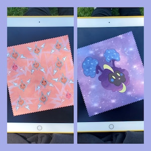 May include: Two microfiber cleaning cloths with different designs. One cloth has a pink and orange background with a repeating pattern of a yellow lightning bolt and a cartoon orange creature. The other cloth has a purple background with a galaxy design and a cartoon purple creature with a yellow face.
