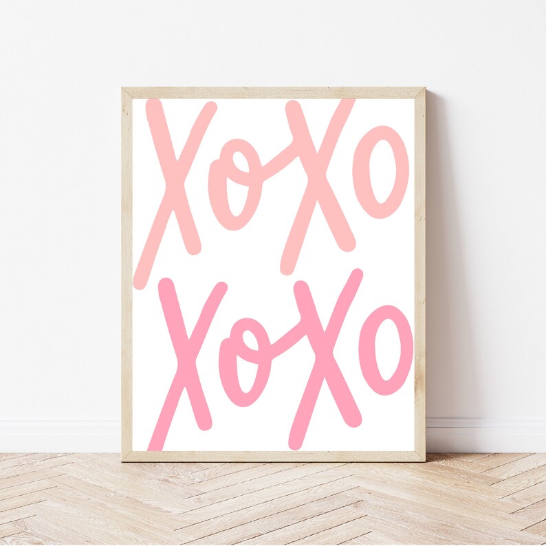 K&ouml;nnte beinhalten: Ein gerahmter Druck mit dem Text "XOXO", der zweimal in Rosa und Hellrosa auf wei&szlig;em Hintergrund wiederholt wird.