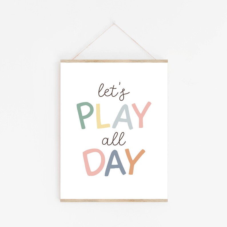 May include: A white framed print with the text "let's PLAY all DAY" in colorful, handwritten letters. The letters are in shades of green, yellow, blue, pink, and orange.