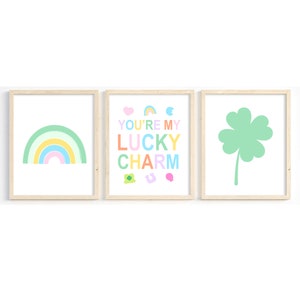 K&ouml;nnte beinhalten: Drei gerahmte Drucke mit einem Regenbogen, einem vierbl&auml;ttrigen Kleeblatt und dem Text "You're my lucky charm" in bunten Buchstaben.