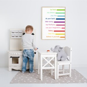 Puede incluir: Una cocina de juguete blanca con una puerta de horno negra y una alfombra de lunares grises. Un ni&ntilde;o est&aacute; jugando con una estufa de juguete. Un p&oacute;ster enmarcado con l&aacute;pices de colores y el texto "be kind, say please, play fair, do your best, take turns, say thankyou, use your imagination, listen, have fun, believe in yourself." est&aacute; colgado en la pared.