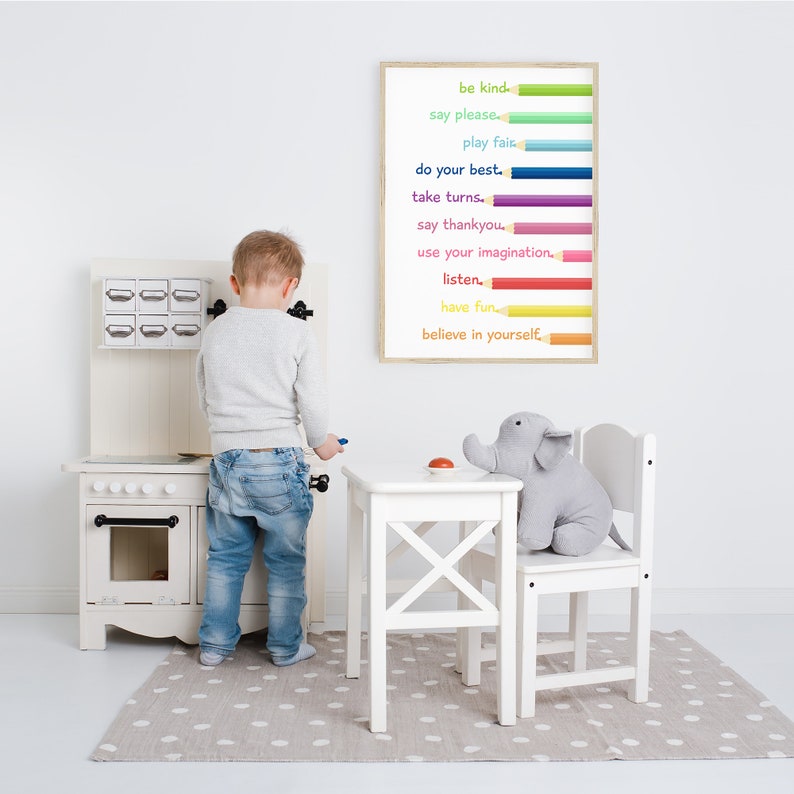 Puede incluir: Una cocina de juguete blanca con una puerta de horno negra y una alfombra de lunares grises. Un ni&ntilde;o est&aacute; jugando con una estufa de juguete. Un p&oacute;ster enmarcado con l&aacute;pices de colores y el texto "be kind, say please, play fair, do your best, take turns, say thankyou, use your imagination, listen, have fun, believe in yourself." est&aacute; colgado en la pared.