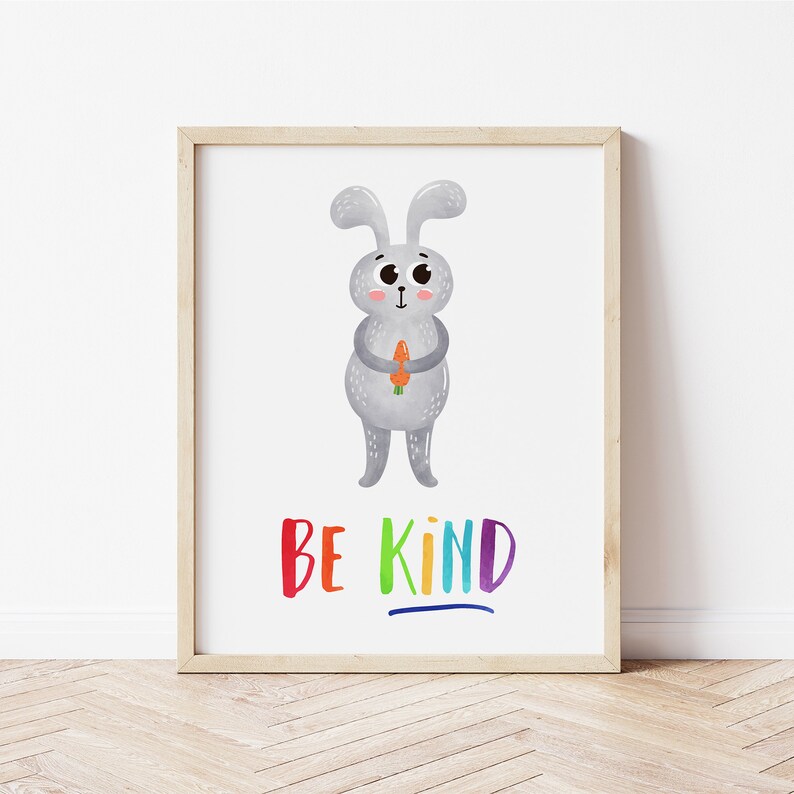 May include: A framed print with a cute cartoon gray bunny holding a carrot. The bunny has big eyes and a pink nose. The text "BE KIND" is written in rainbow colors below the bunny.