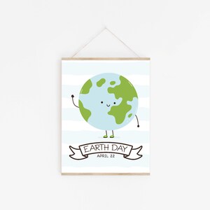 May include: A framed Earth Day print featuring a smiling Earth with green continents and a light blue ocean. The print includes the text "Earth Day April 22" on a banner, set against a backdrop of blue and white stripes.