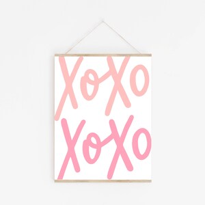 K&ouml;nnte beinhalten: Ein wei&szlig;er gerahmter Druck mit dem Text "XOXO", der zweimal in Rosa und Hellrosa wiederholt wird.