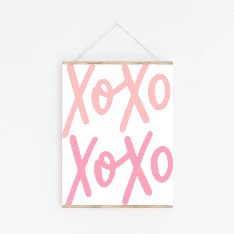 K&ouml;nnte beinhalten: Ein wei&szlig;er gerahmter Druck mit dem Text "XOXO", der zweimal in Rosa und Hellrosa wiederholt wird.