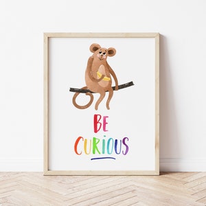 May include: A framed print with a cartoon monkey sitting on a branch and eating a banana. The text "BE CURIOUS" is written in rainbow colors below the monkey.