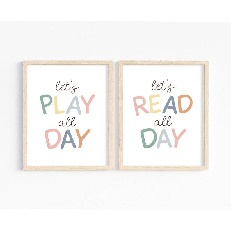 May include: Two framed prints with a white background and light wood frames. The text on the prints reads "let's play all day" and "let's read all day" in colorful, stylized letters.