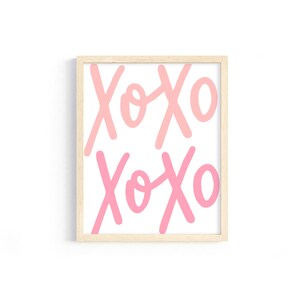 K&ouml;nnte beinhalten: Ein gerahmter Druck mit dem Text "XOXO", der zweimal in einem rosa und hellrosa Farbverlauf wiederholt wird. Der Rahmen ist in hellem Holz gehalten.