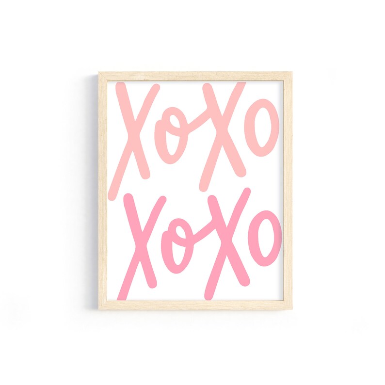 K&ouml;nnte beinhalten: Ein gerahmter Druck mit dem Text "XOXO", der zweimal in einem rosa und hellrosa Farbverlauf wiederholt wird. Der Rahmen ist in hellem Holz gehalten.