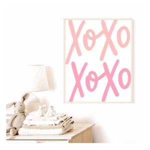 K&ouml;nnte beinhalten: Ein gerahmter Druck mit dem Wort "XOXO", das zweimal in rosa und wei&szlig;en Buchstaben auf wei&szlig;em Hintergrund geschrieben ist.