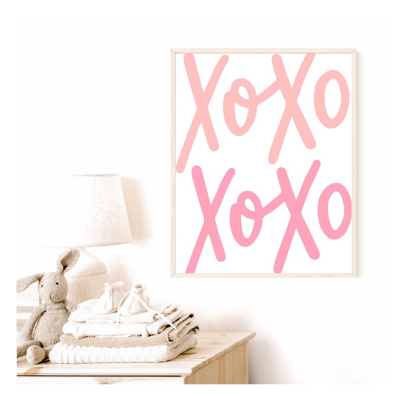 K&ouml;nnte beinhalten: Ein gerahmter Druck mit dem Wort "XOXO", das zweimal in rosa und wei&szlig;en Buchstaben auf wei&szlig;em Hintergrund geschrieben ist.