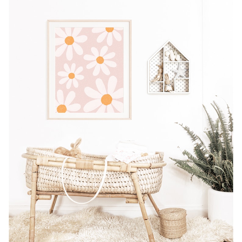 May include: A white wicker bassinet with a white blanket and a stuffed bunny inside. The bassinet is on a white rug in front of a white wall with a framed print of orange and white daisies and a white shelf with a house-shaped design.
