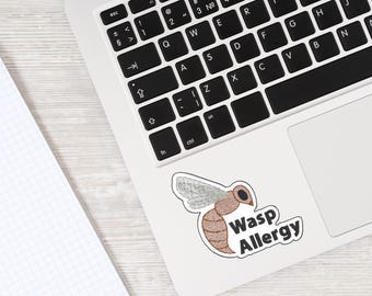 May include: A sticker featuring a cartoon wasp with the text "Wasp Allergy." The sticker is on a white laptop, next to a notebook. The wasp is brown and tan with gray wings.