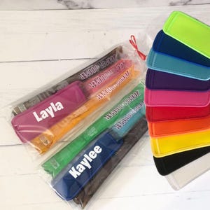 Puede incluir: Una colección de coloridos portahielos personalizados en varios colores, incluyendo rosa, naranja, verde y azul. Cada portahielos tiene un nombre impreso. También se ve una pila de portahielos a juego en diferentes colores.