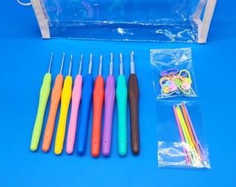 May include: A collection of colorful crochet hooks with ergonomic handles, arranged with a clear zippered pouch, stitch markers, and yarn needles on a blue background. The hooks come in various colors, including yellow, pink, and green.