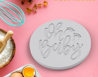 Puede incluir: Un molde de silicona blanco para hornear galletas con el texto "oh baby" y dos pequeñas huellas de pies.