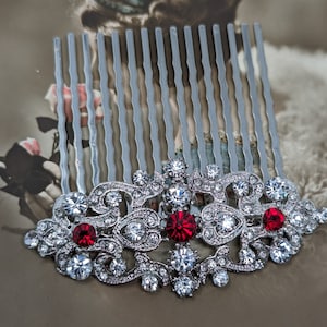 May include: Silver hair comb with a decorative design featuring clear and red rhinestones. The comb has a silver metal base with a row of teeth.