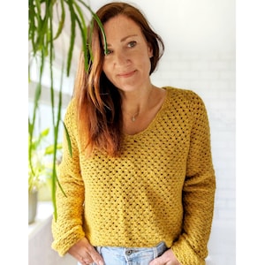 Könnte beinhalten: Eine Frau trägt einen gelben Häkelpullover mit einem lockeren, offenen Stichmuster. Der Pullover hat einen V-Ausschnitt und lange Ärmel.