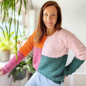 May include: A colorful crocheted sweater with a pink, orange, green, and purple color block design. The sweater has a round neckline and long sleeves.