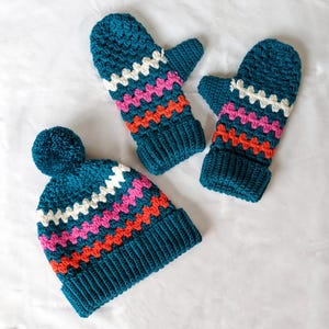 May include: A teal blue crocheted hat with a white pom pom and colorful stripes. Two matching teal blue crocheted mittens with colorful stripes.