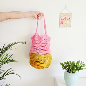 May include: A pink and yellow crocheted tote bag with a mesh design. The bag is hanging from a hand.