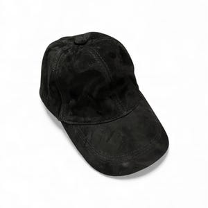 May include: A black baseball cap with a curved brim. The cap is made of a soft, suede-like material and features a button on top. The hat is a solid black color and is suitable for casual wear.