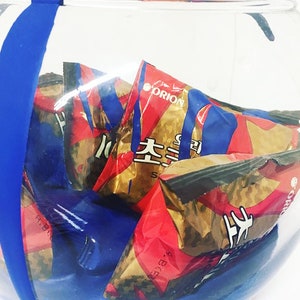 May include: A glass bowl filled with multiple red and gold snack bags. The bags have Korean text and the word "Orion" printed on them.