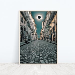 May include: A cobblestone street lined with buildings, leading to a view of a solar eclipse in the sky.